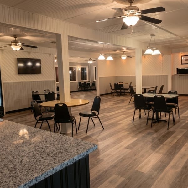 Spacious, clean restaurant dining room with black tables, chairs, wood-look floor, and ceiling fans.