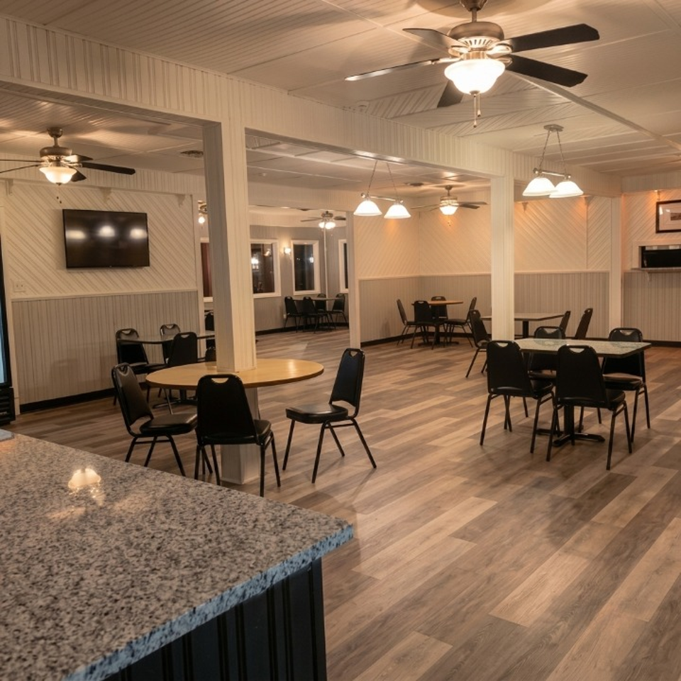 Spacious, clean restaurant dining room with black tables, chairs, wood-look floor, and ceiling fans.