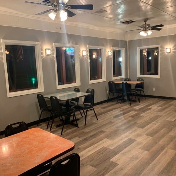 Empty restaurant dining room with several tables, chairs, windows, and ceiling fans.