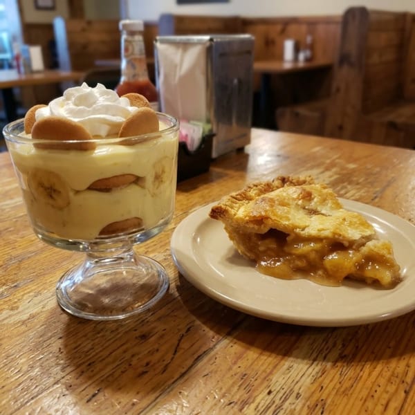 Banana pudding and a slice of pie on a rustic wooden table in a restaurant.